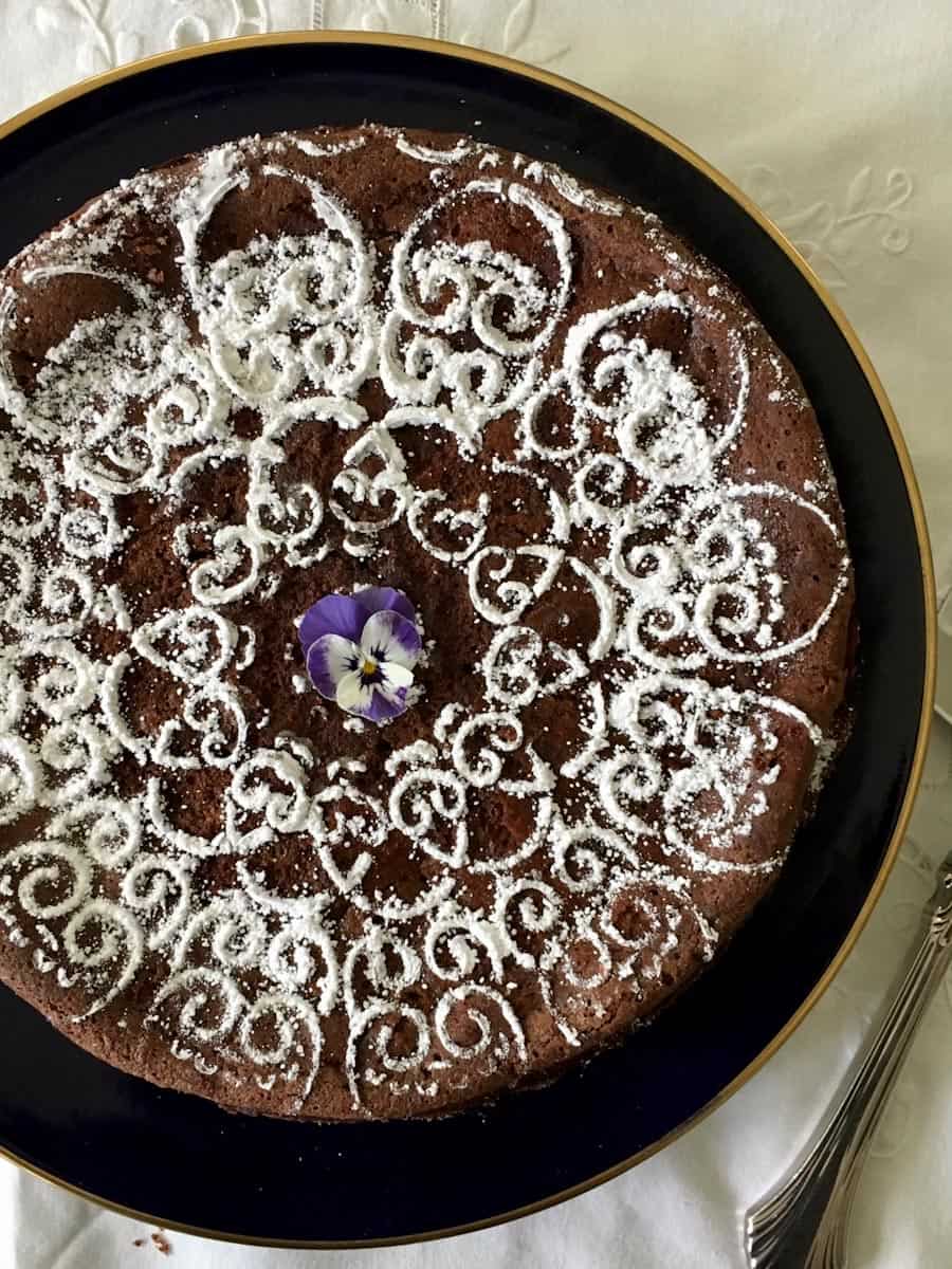 Whole chocolate cake with powdered sugar design on a plate with a server.