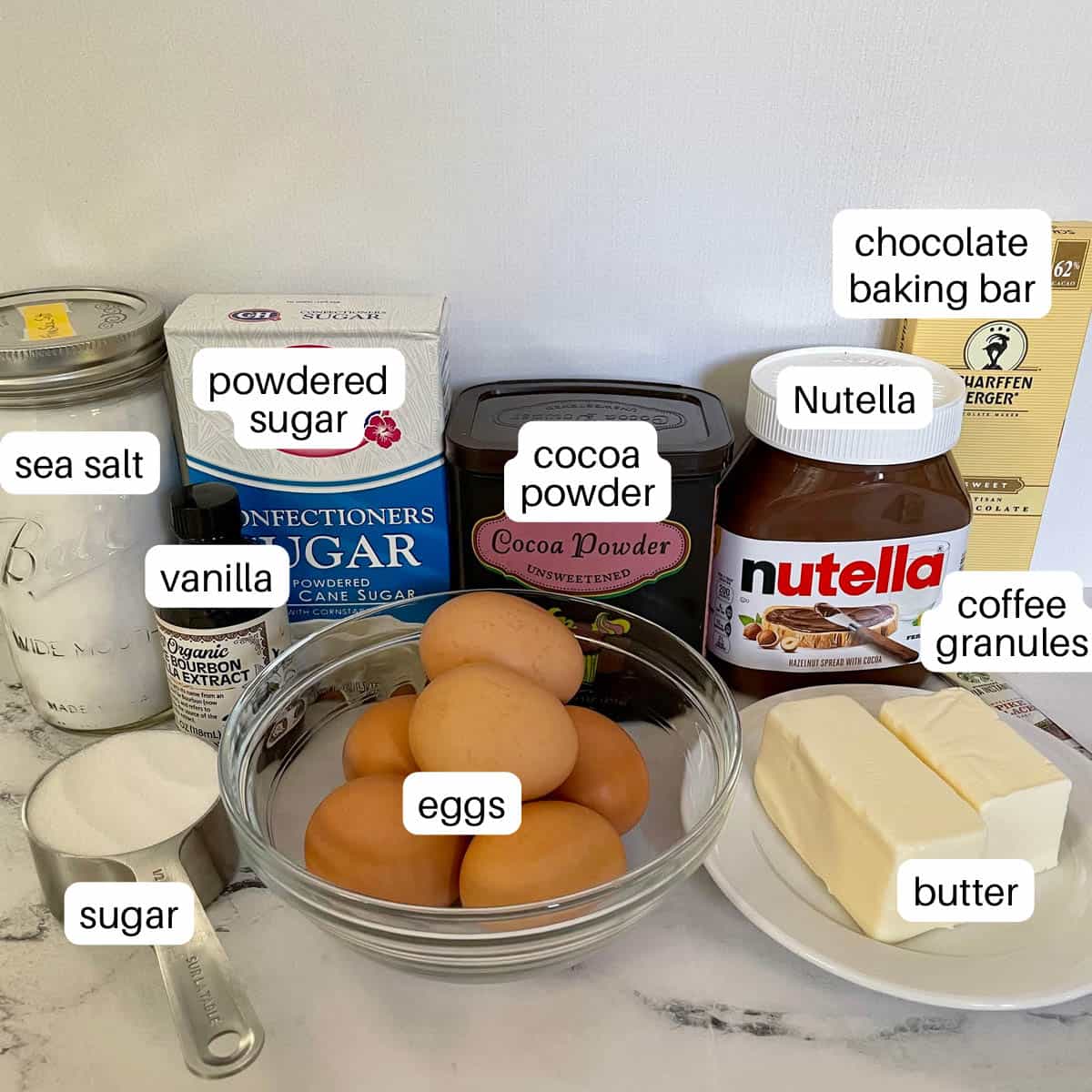 Ingredients for cake including sugar, eggs, butter, salt, vanilla, powdered sugar, cocoa, Nutella, coffee, and chocolate. 