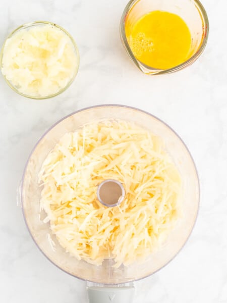 Shredded potatoes, finely chopped onion, and beaten eggs in glass containers on the counter.