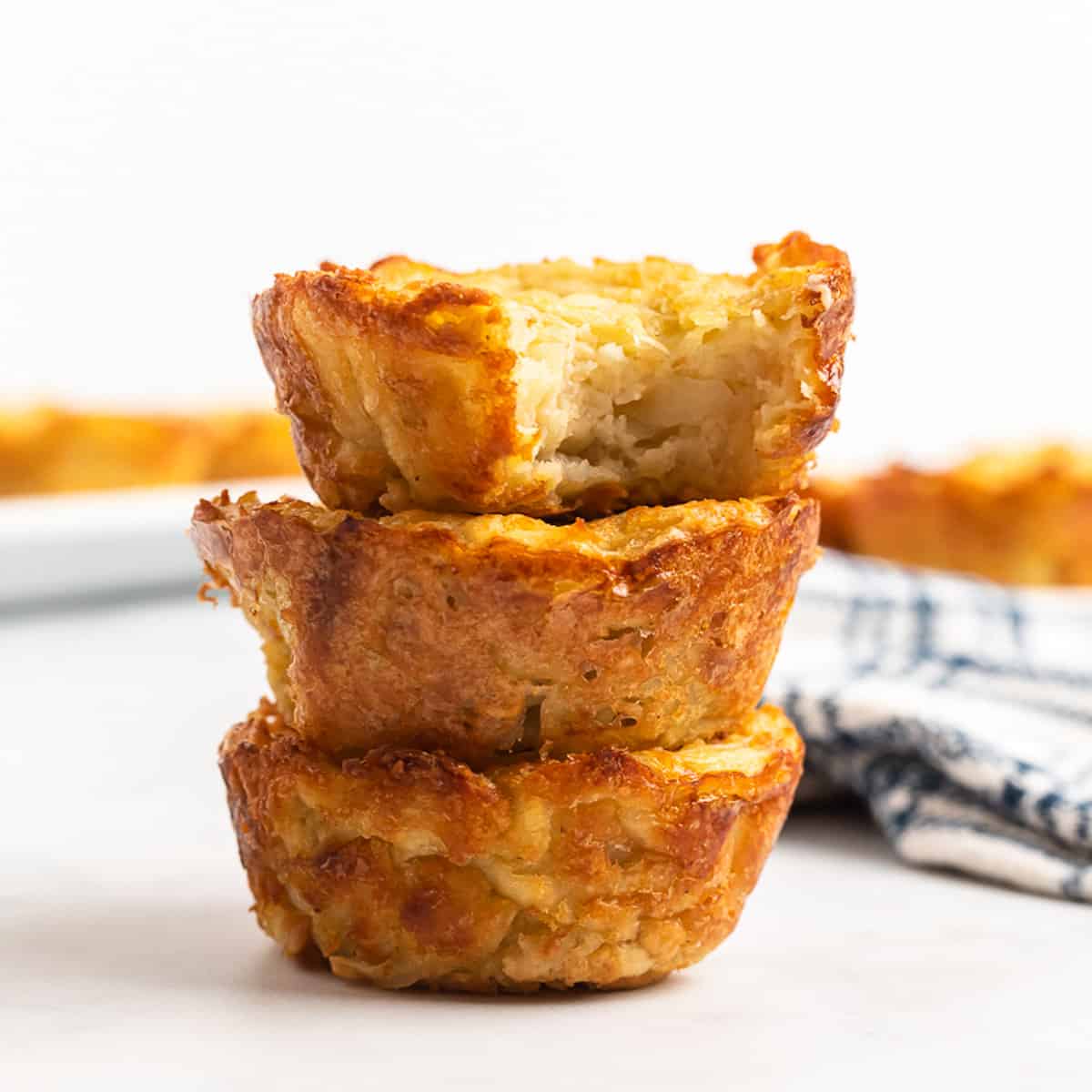 Stack of 3 potato latke muffins with a bite showing the inside.