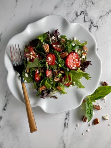 Strawberry salad with baby greens, pecans, feta cheese, and strawberries on a plate with a fork.