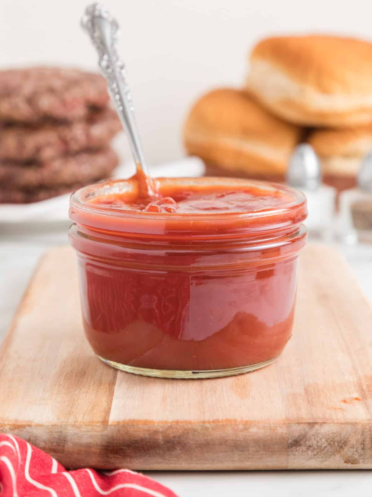 Jar of hickory barbecue sauce with hamburger in the background.