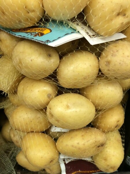 Baby Yukon gold potatoes in a net bag on market shelf.