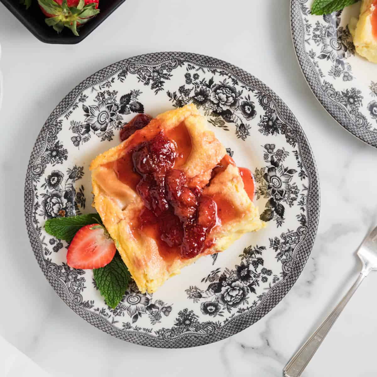 A slice of blintz souffle casserole on a plate with strawberry jam.