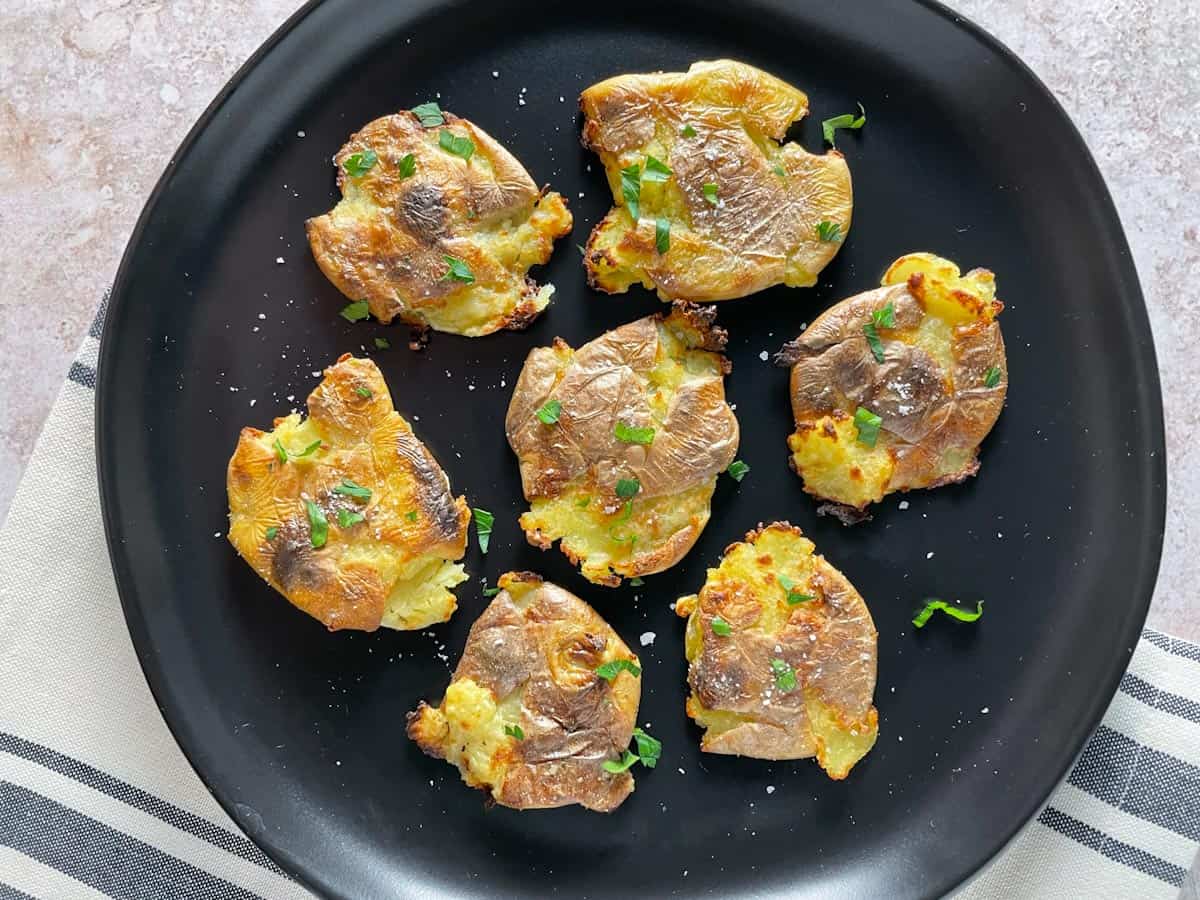 Smashed potatoes on a black plate.