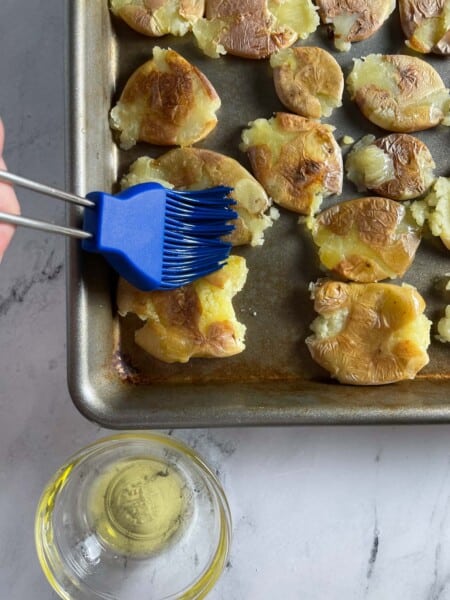 Brushing oil on potatoes in a pan.