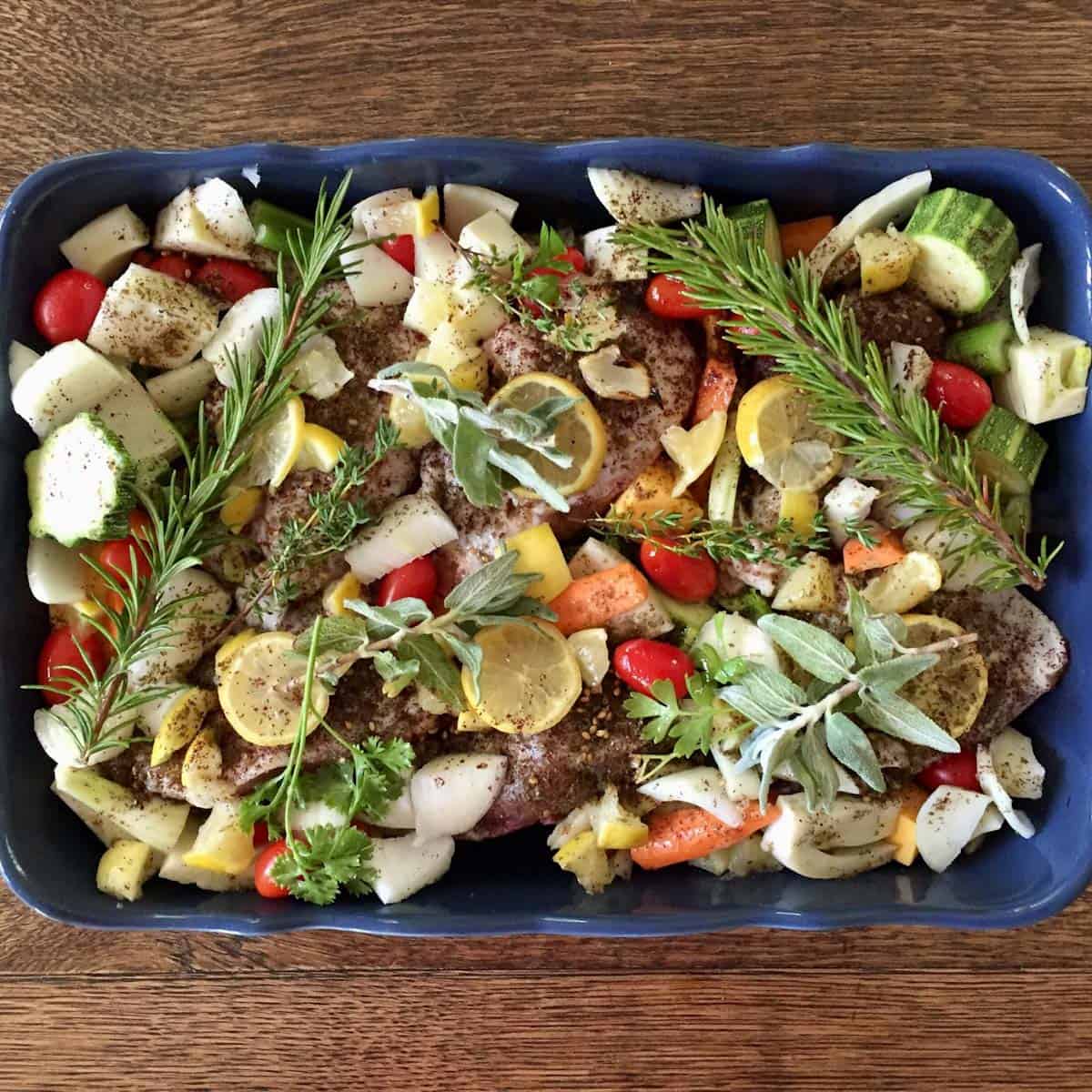 Lemon herb chicken with za'atar, sumac, onion, and vegetables in a blue baking dish.