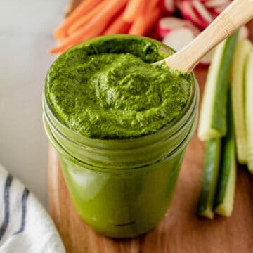 A jar of bright green tahini sauce with a wooden spoon.