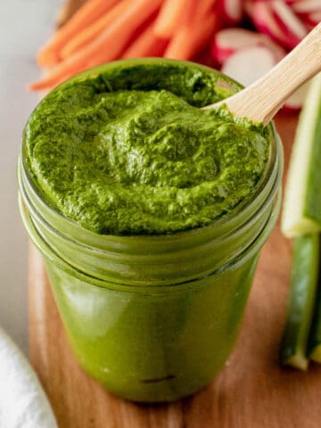 A jar of bright green tahini sauce with a wooden spoon.