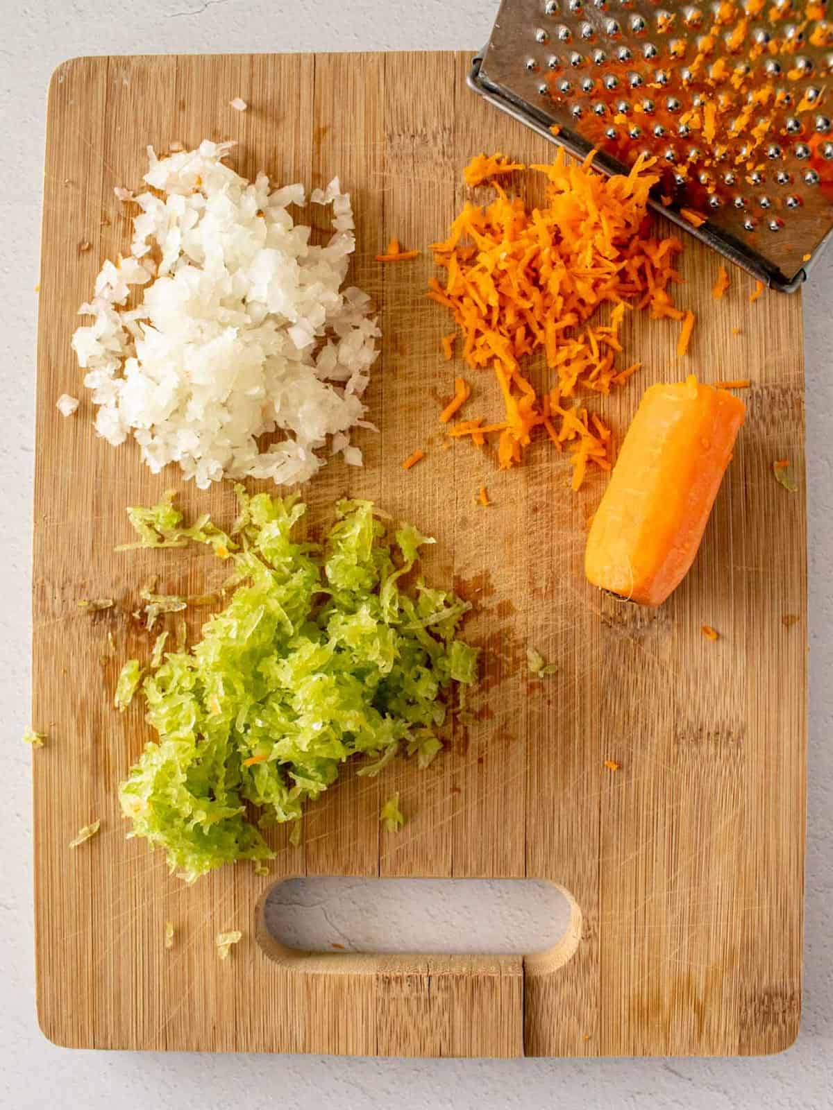 Grated onions, carrots, and celery on cutting board, a soffritto mix of vegetables.