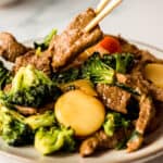 Chinese beef and vegetable stir fry on a plate with one piece held above by a chopstick.
