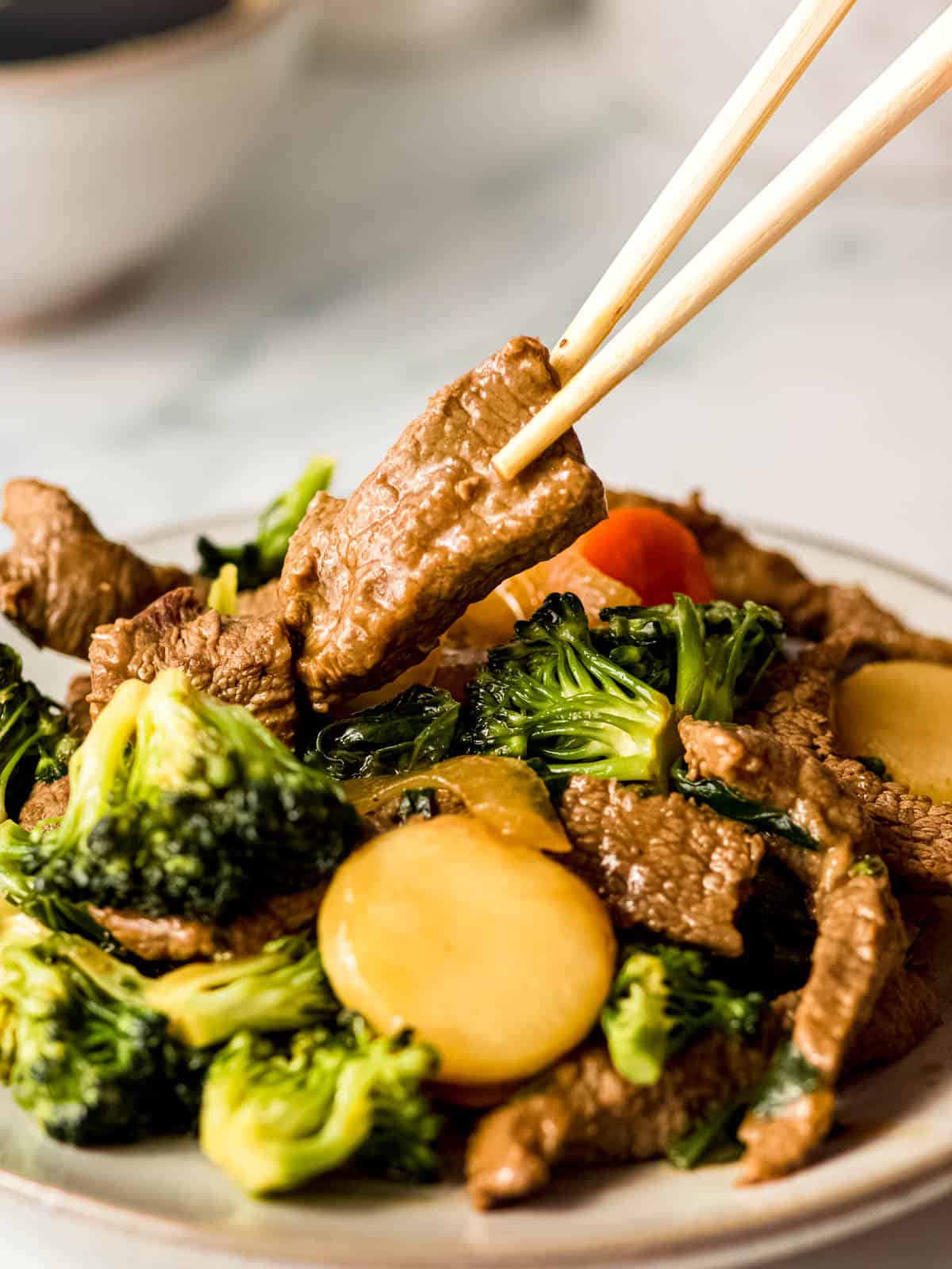 Chinese beef and vegetable stir fry on a plate with one piece held above by a chopstick.