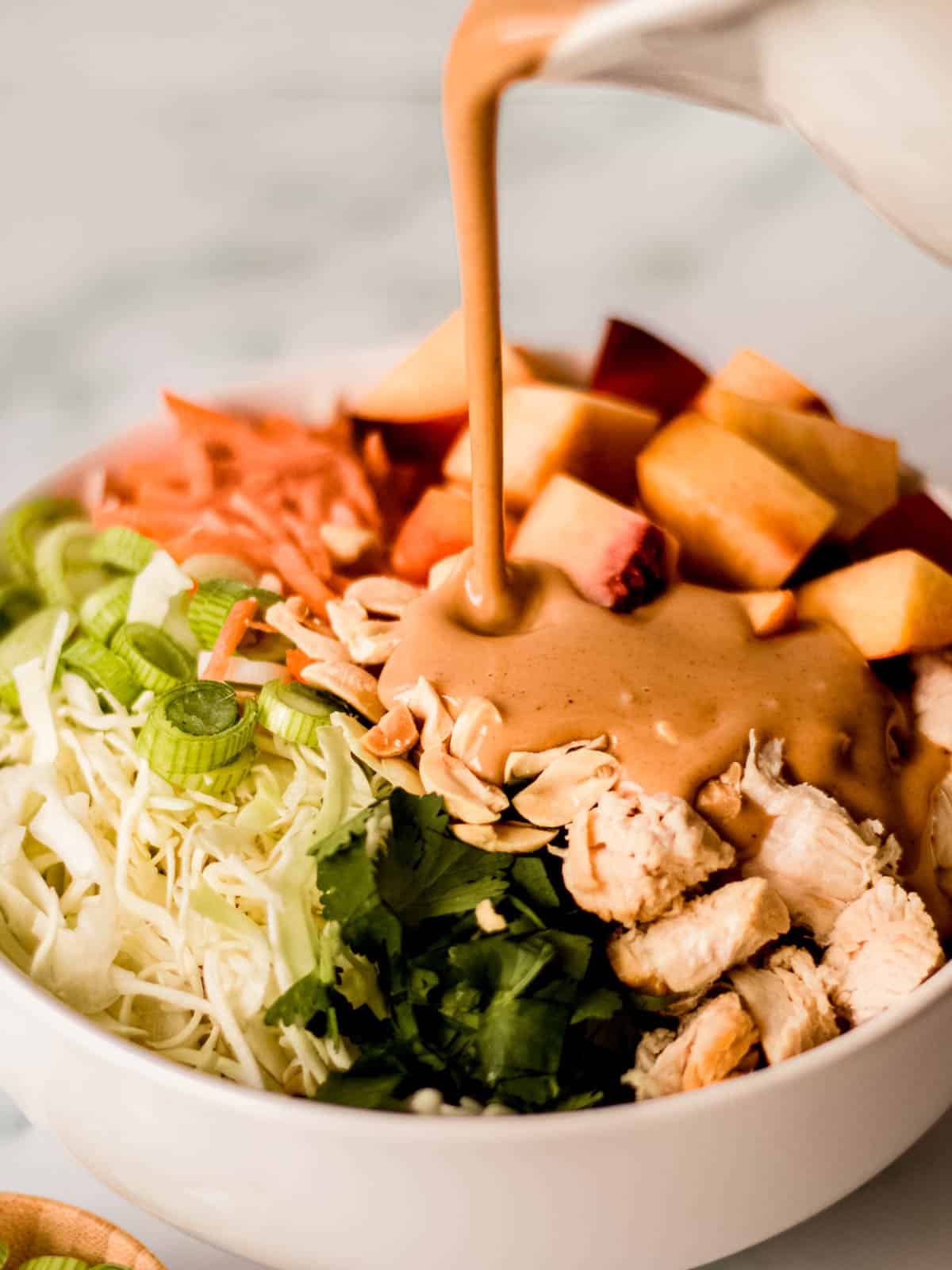 Thai chicken salad with ingredients chopped and peanut dressing being poured.