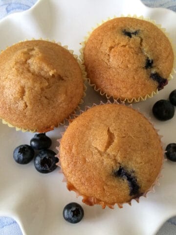Maple syrup and blueberry pancake muffins on a plate with a few blueberries scattered around.