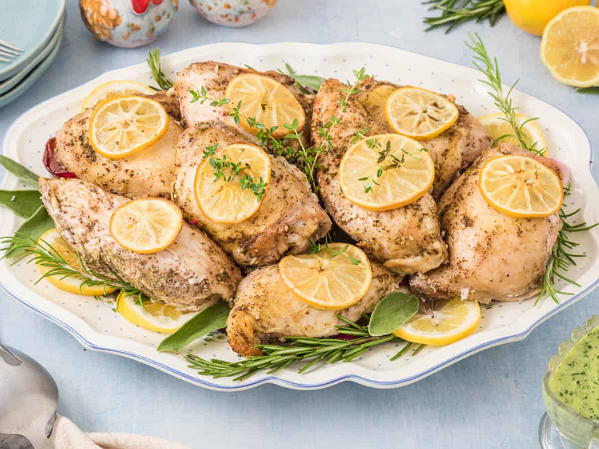 A platter of za'atar chicken breasts garnished with lemon and herbs.