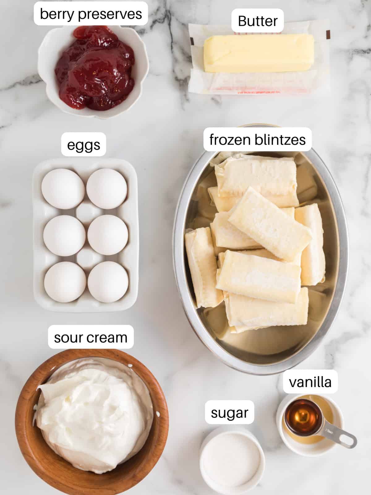 Ingredients for blintz souffle in little bowls including frozen blintzes, cream cheese, and eggs.