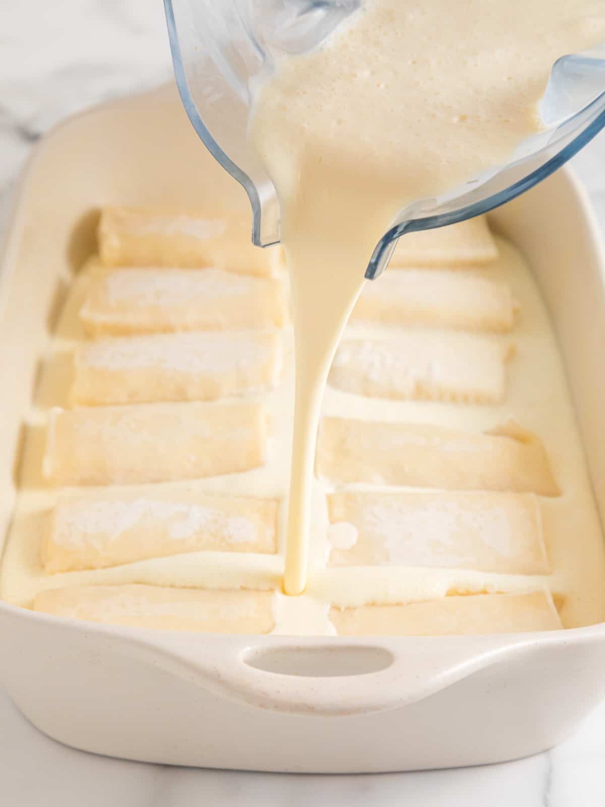 Blintzes lined up in the casserole with souffle batter being poured over.