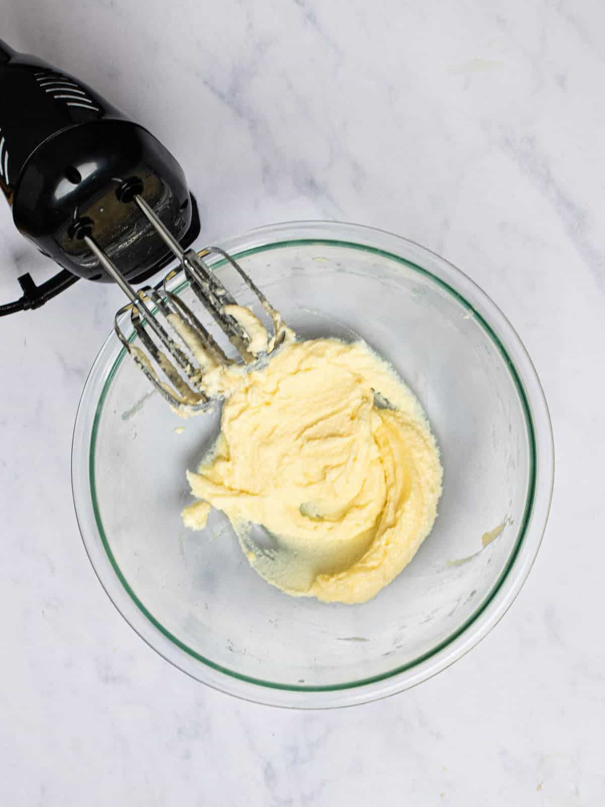 Sugar and butter combined in a glass bowl with hand mixer.