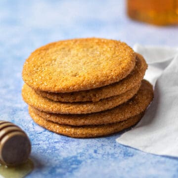 A stack of honey cookies next to a honey dipper on blue background.