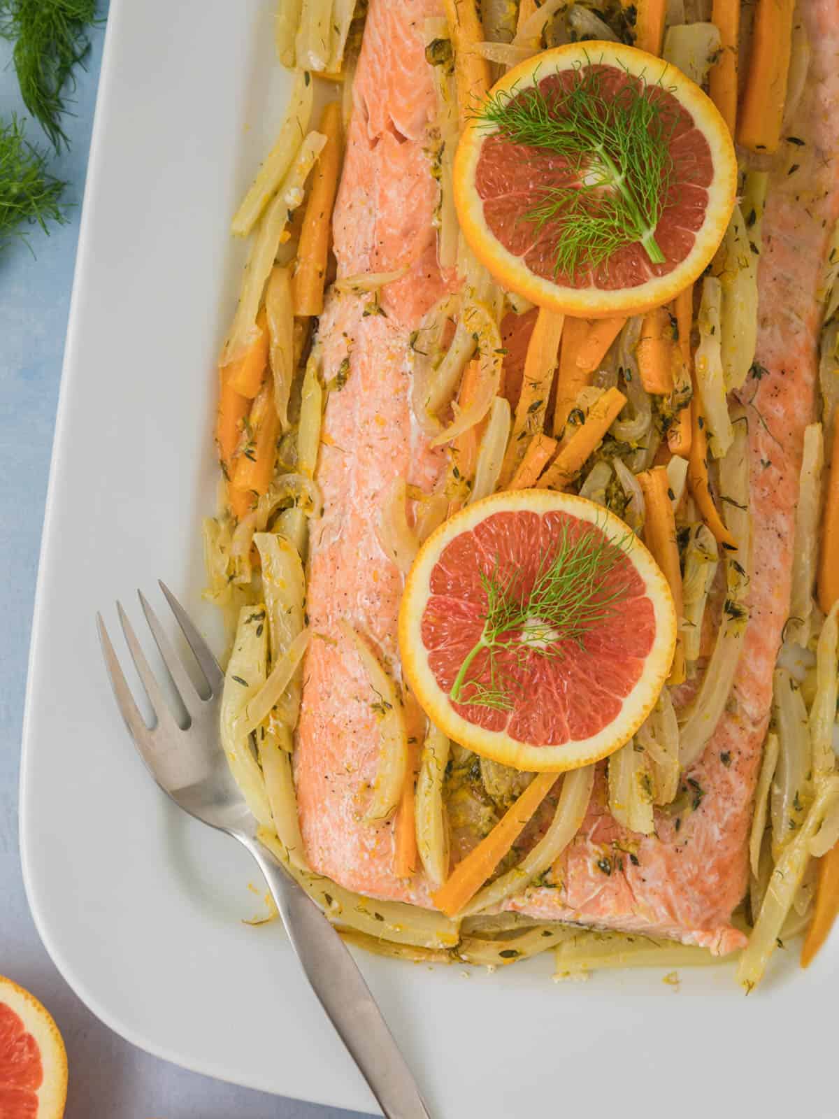 Foil roasted salmon with fennel topped with orange slices on a baking sheet.