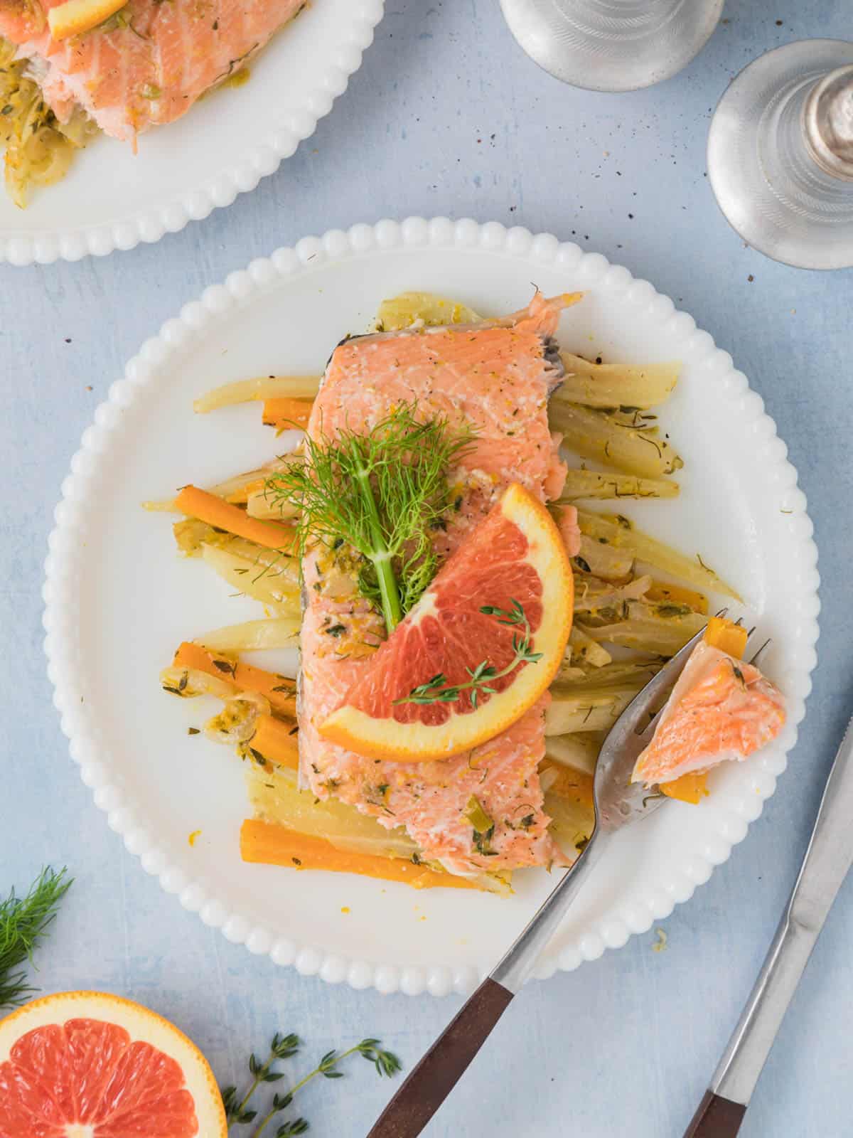 Salmon with carrots and fennel on a white plate topped with fresh herbs.