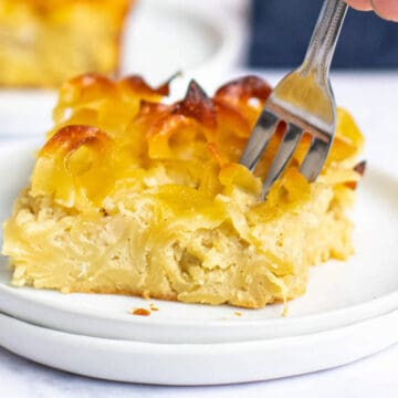 A square of noodle kugel on a plate with a fork starting to scoop a bite.