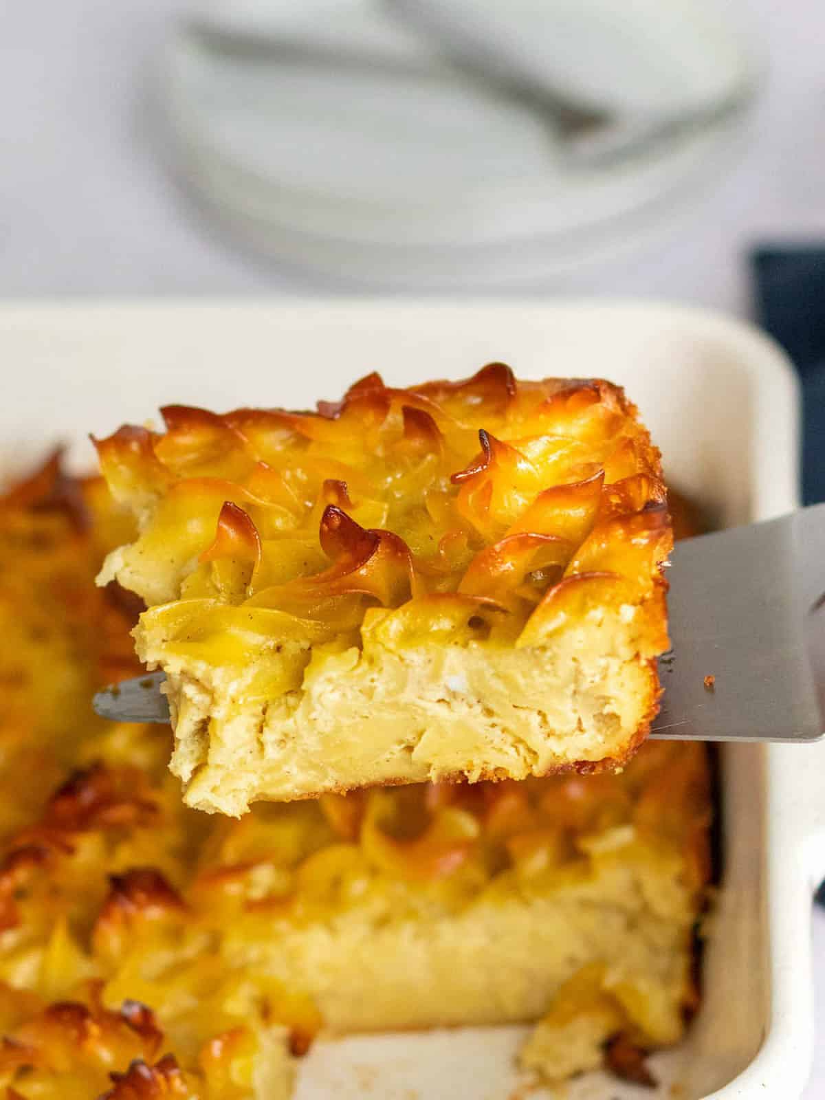 A noodle kugel serving on a spatula with the remaining casserole in the background.
