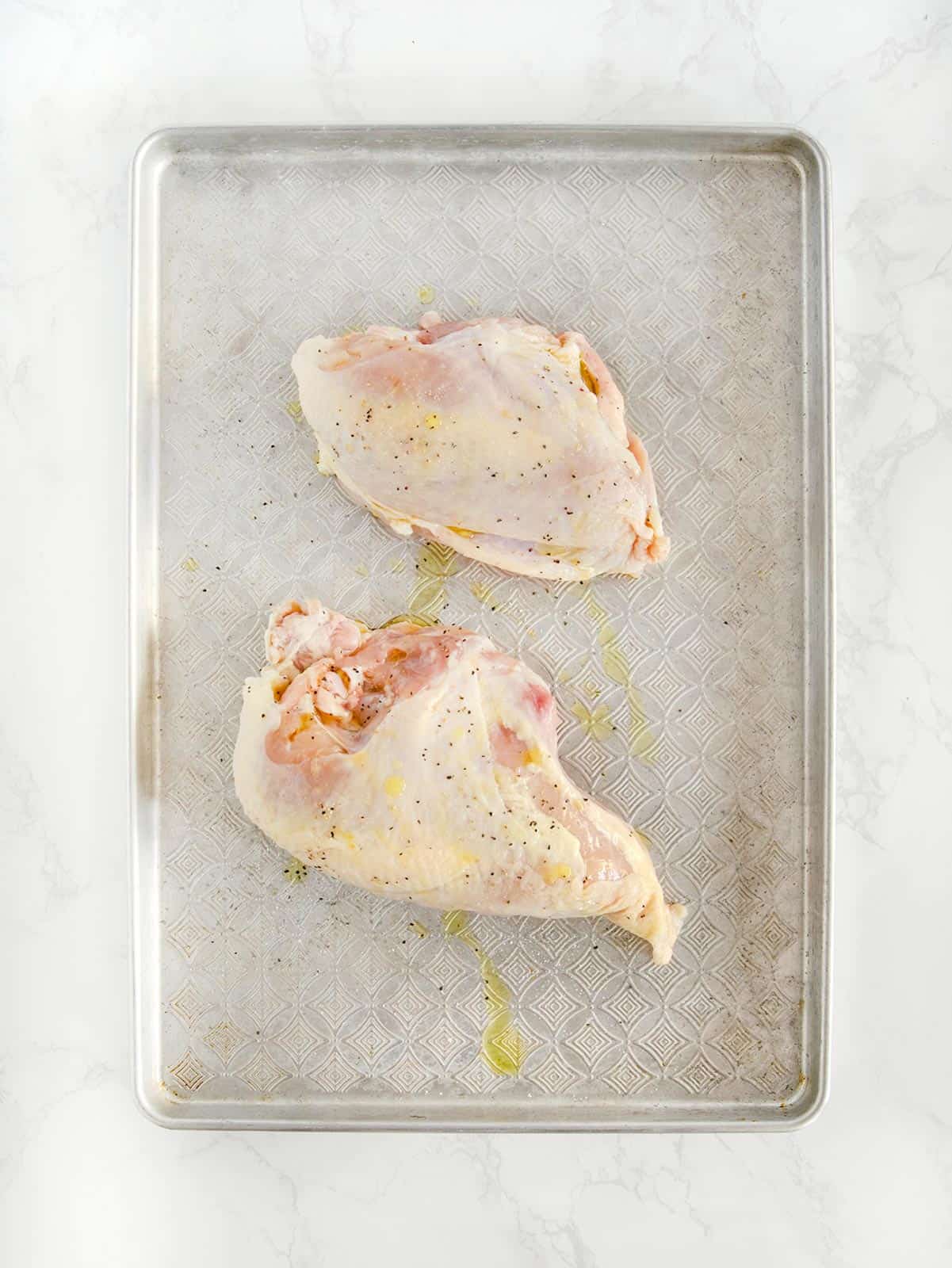 Chicken breasts on a sheet pan with salt, pepper, and olive oil. 