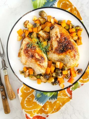Honey mustard chicken on plate with butternut squash, apples, and Brussels sprouts with silverware and napkin.