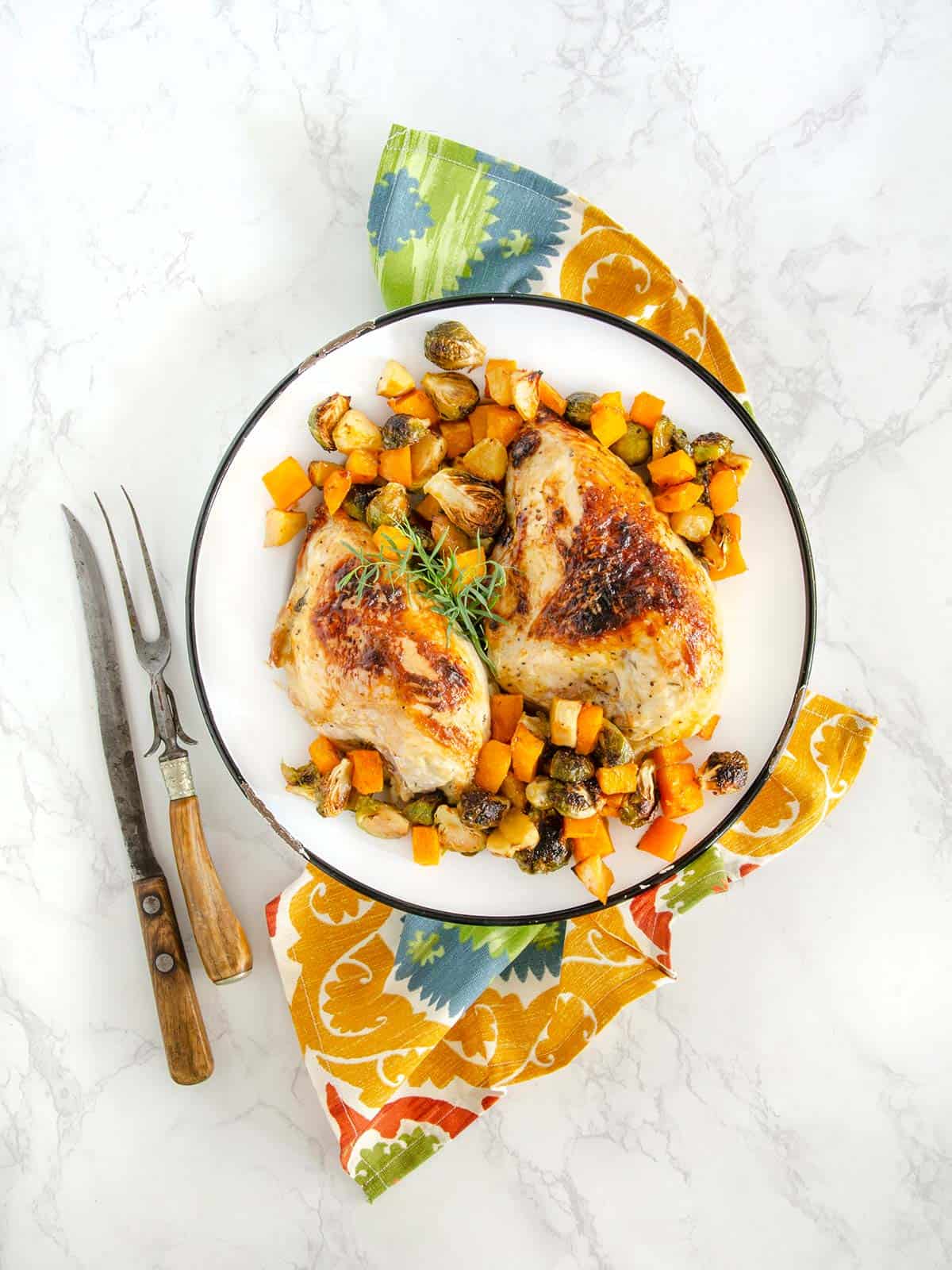 Honey mustard chicken on a plate with veggies next to a decorative napkin and silverware.