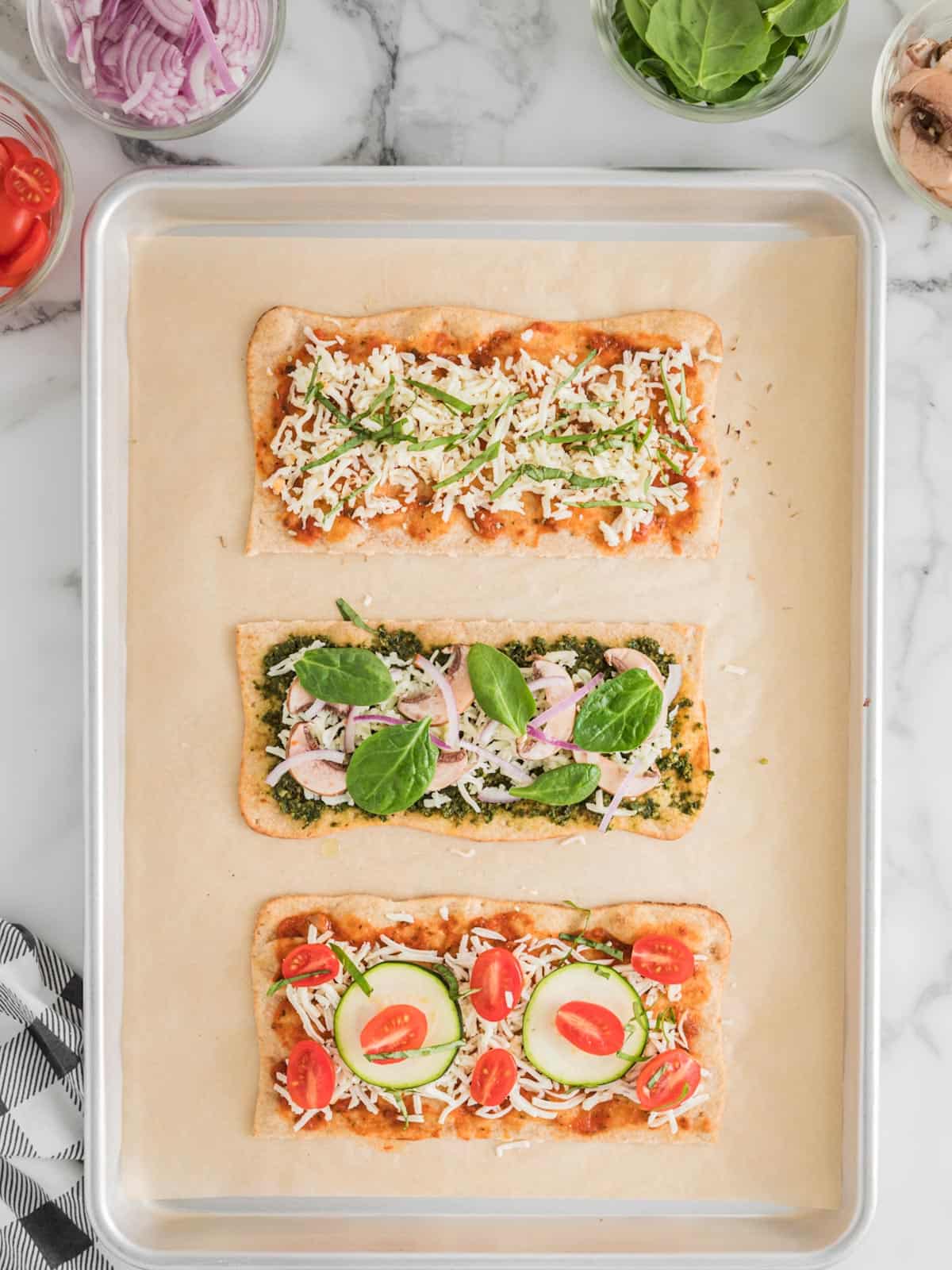 Sheet pan with three versions of lavash pizza with different toppings ready for the oven.
