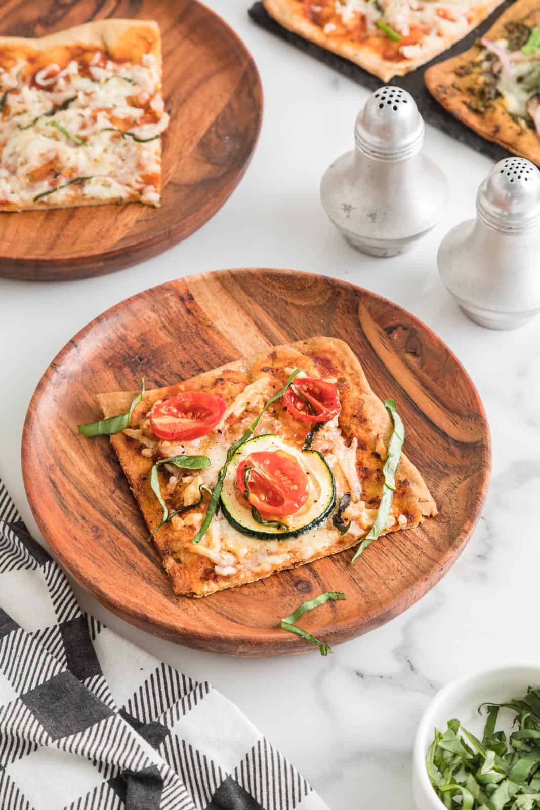 Slice of lavash pizza with zucchini, cherry tomato, and basil toppings served on wood plate.
