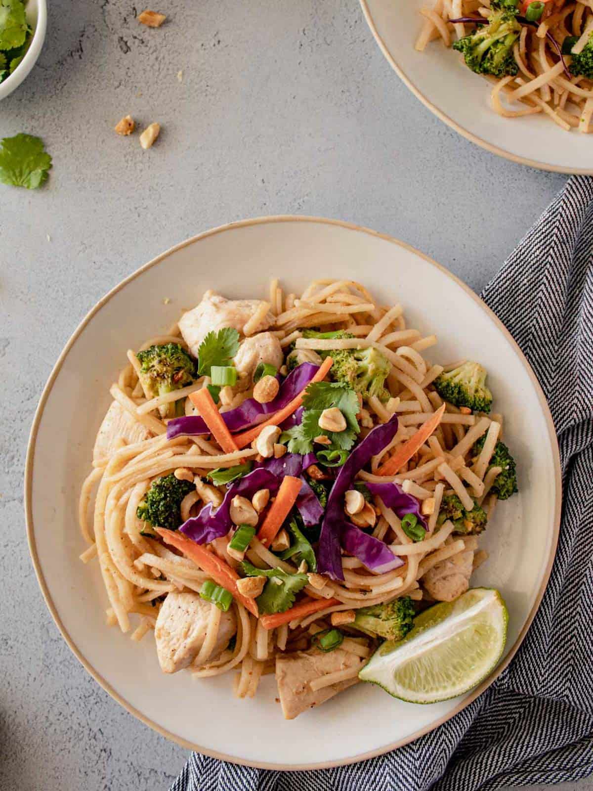 Chicken pad Thai on a plate topped with peanuts and lime .