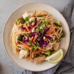 Chicken pad Thai on a plate topped with peanuts and lime .