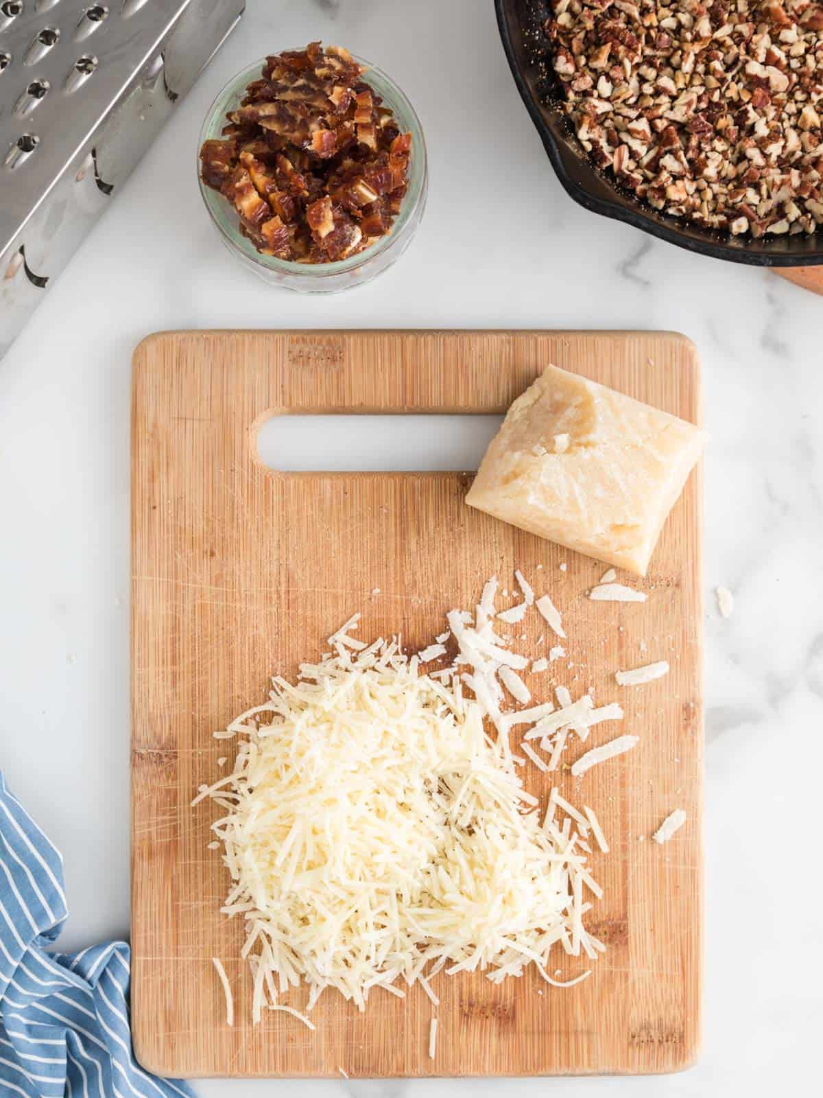 Grated parmesan on cutting board with chopped dates and pecans ready to go in salad.
