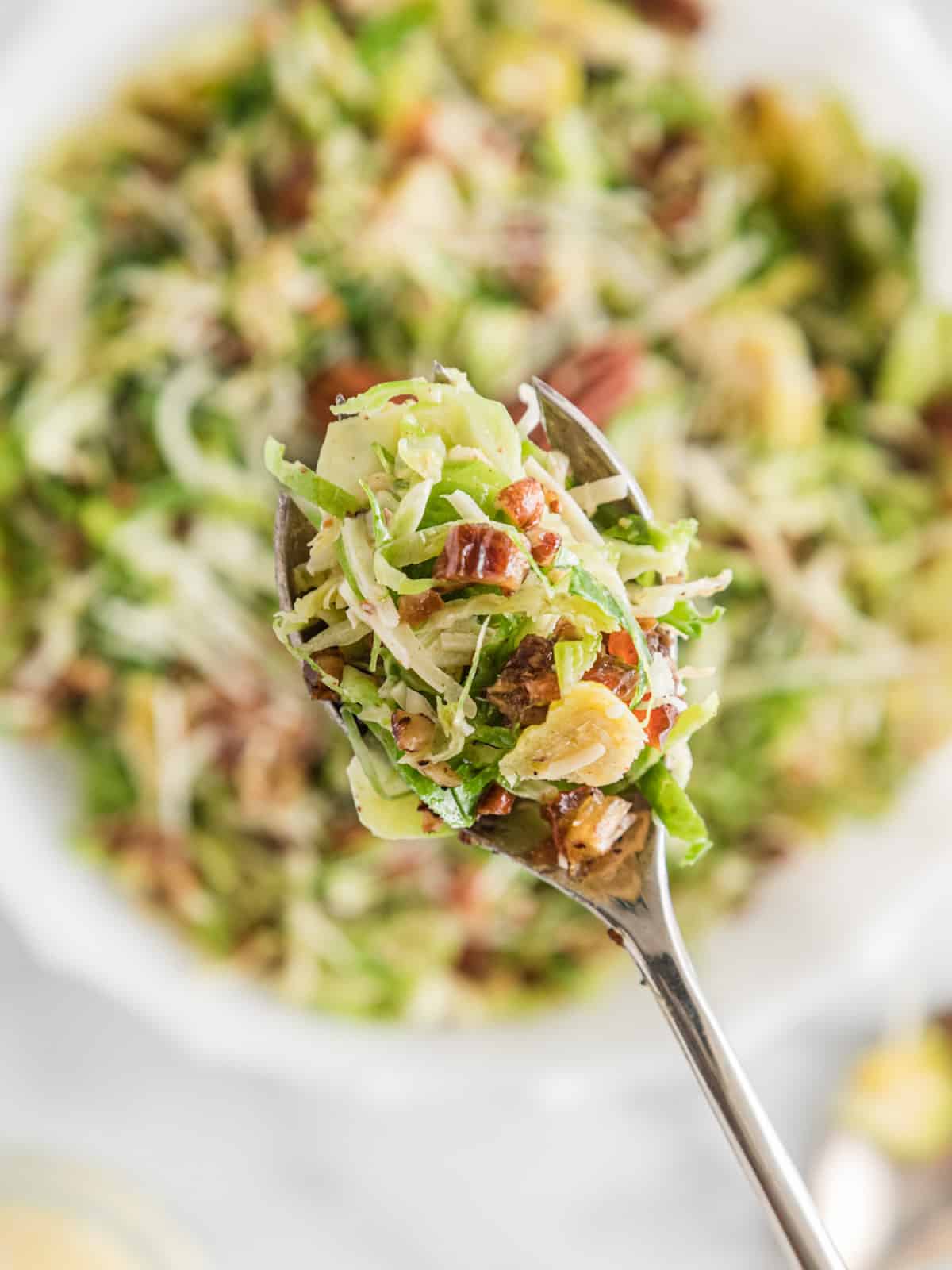Spoonful of shaved Brussels sprouts salad with dates, pecans, and parmesan cheese.