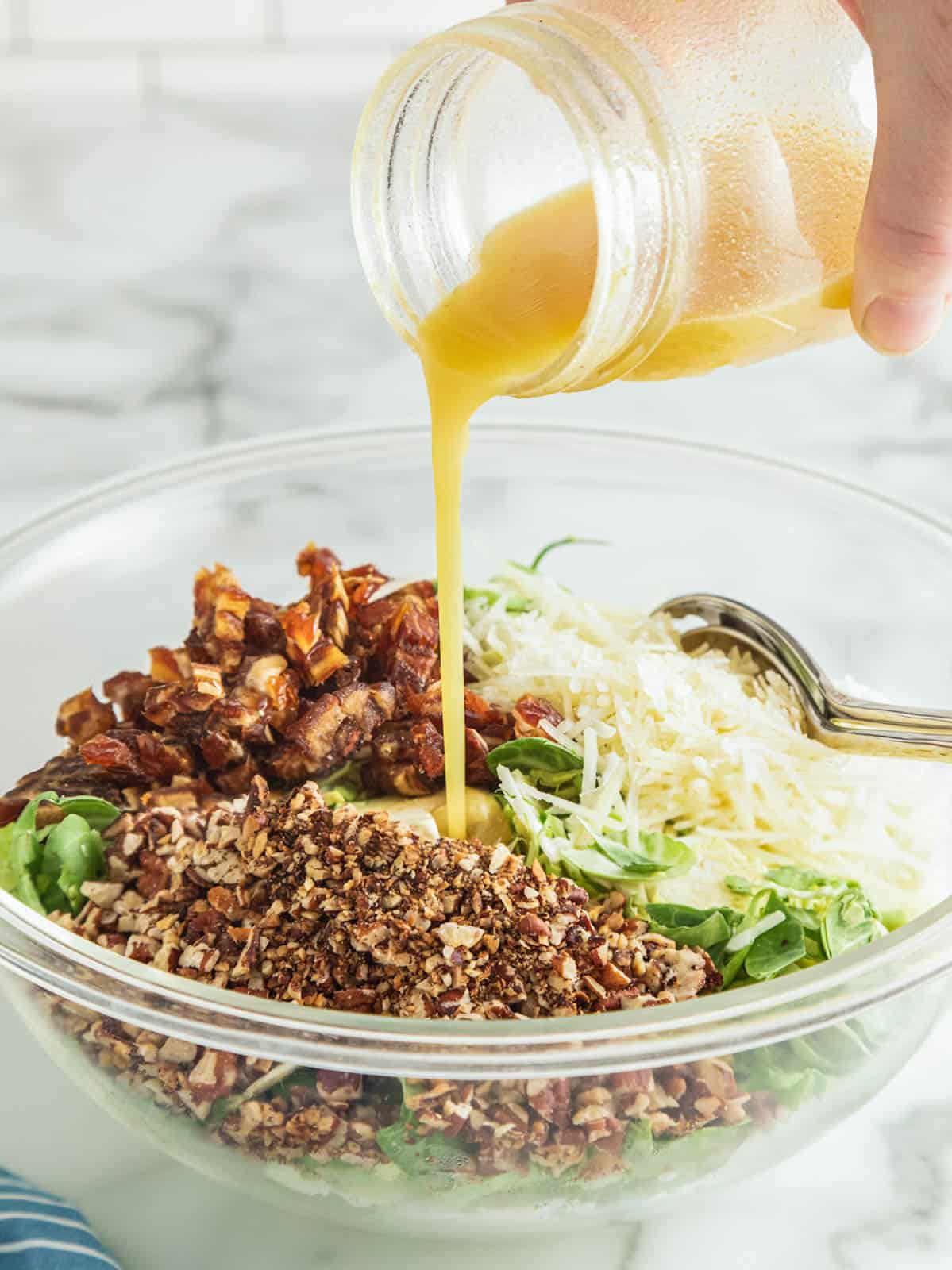 Mustard vinaigrette dressing being poured over salad with chopped dates, pecans, and cheese.