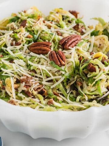 Shaved Brussels sprouts salad with parmesan and pecans in white bowl with spoon.