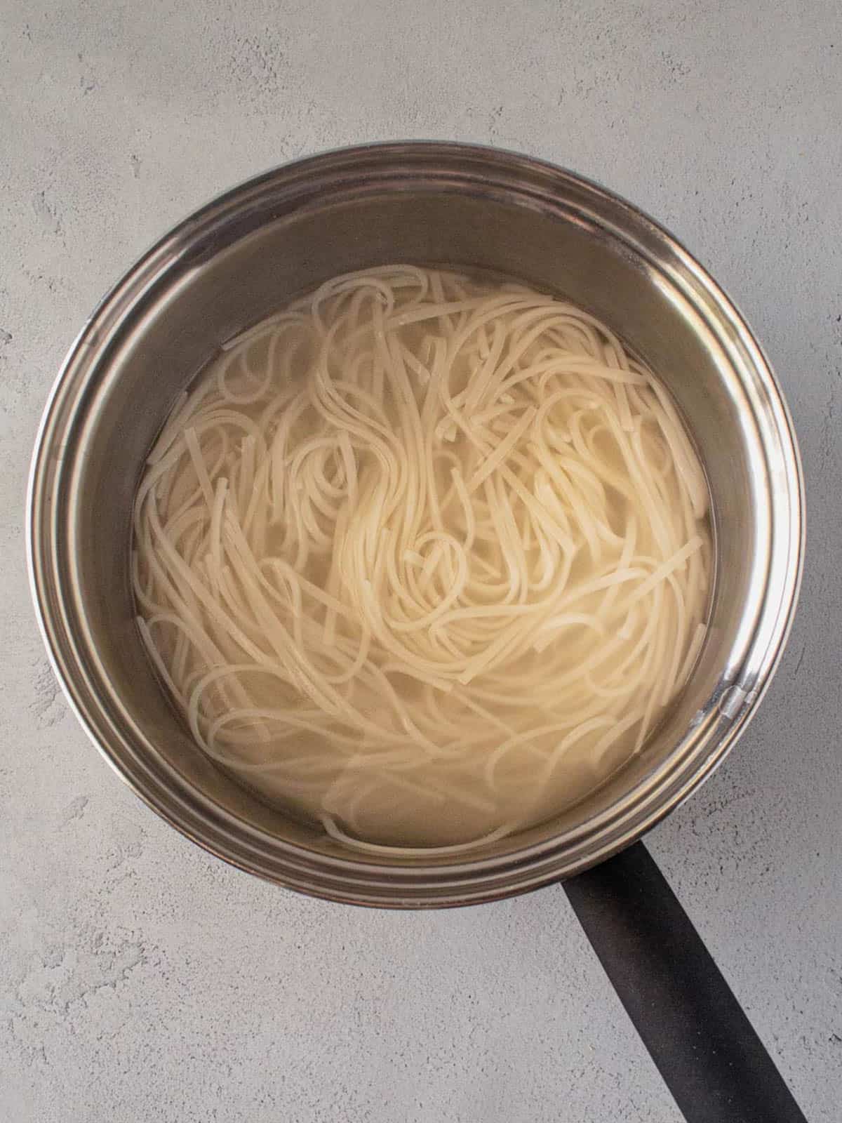 Rice noodles soaking in a pot of water.