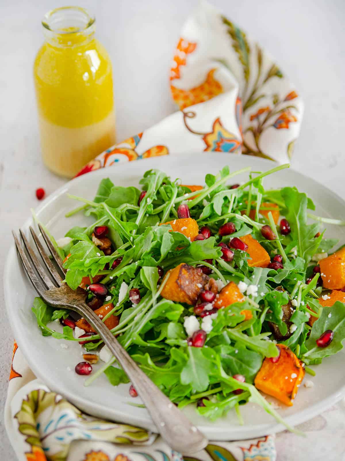 A plate of arugula and butternut squash salad next to a bottle of citrus vinaigrette.