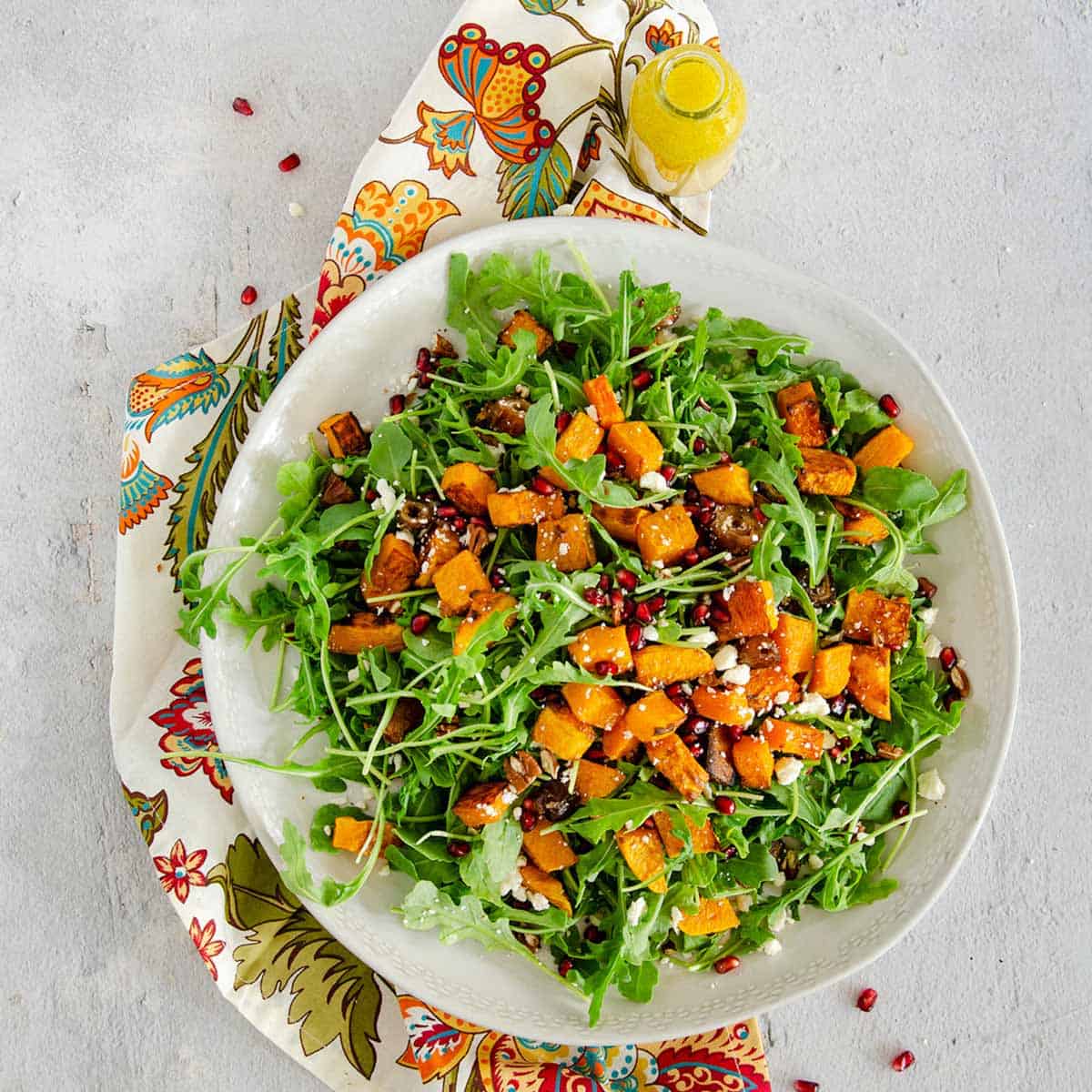A bowl of arugula and roasted butternut squash salad with orange dressing.