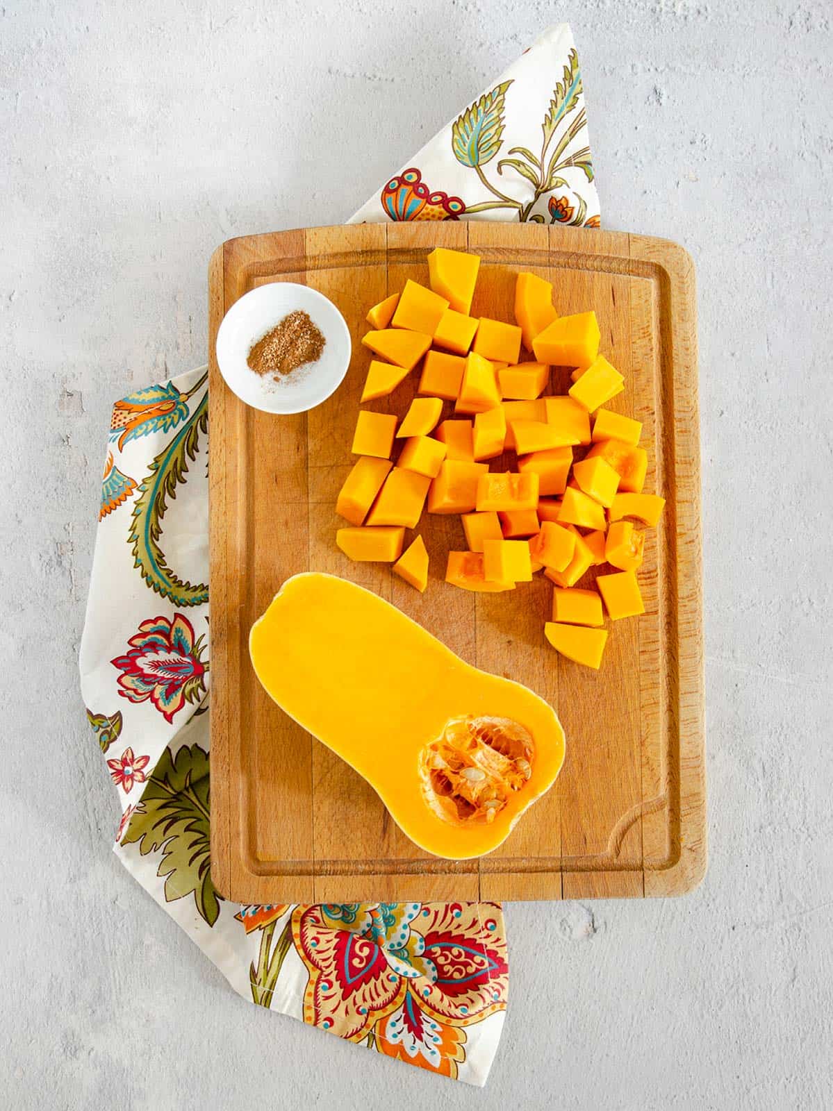 A half butternut squash on a cutting board with the other half cut into cubes.