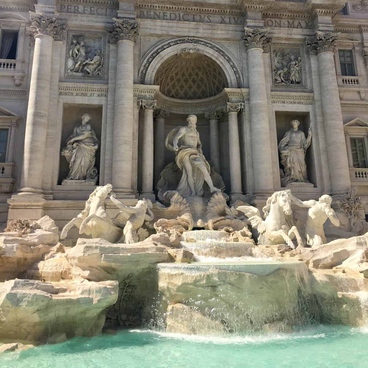 Close up of the Trevi Fountain showing central columns, carved winged horses and people, and water.