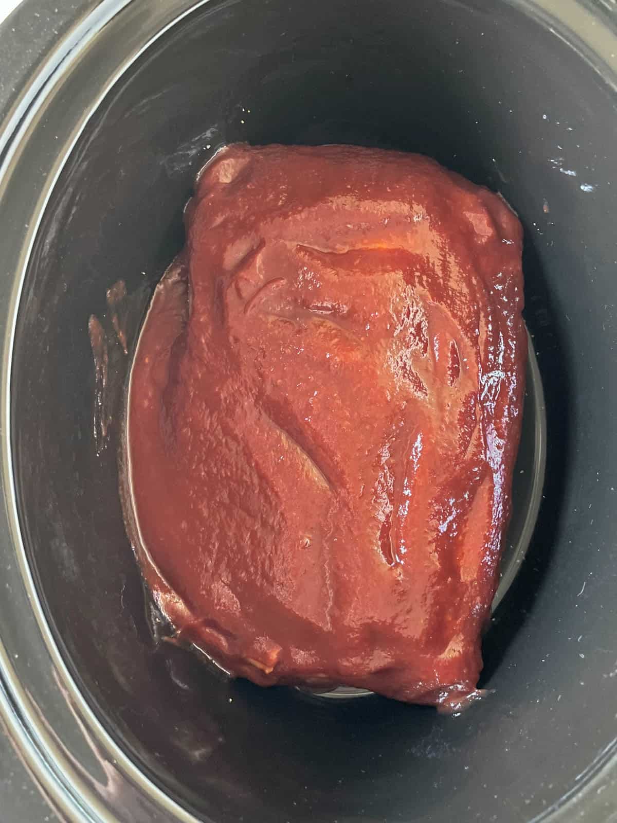 A beef brisket coated in BBQ sauce in a slow cooker.