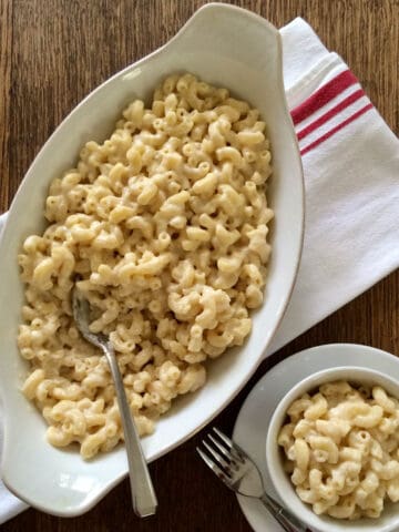A white casserole dish and small bowl filled with creamy mac and cheese.
