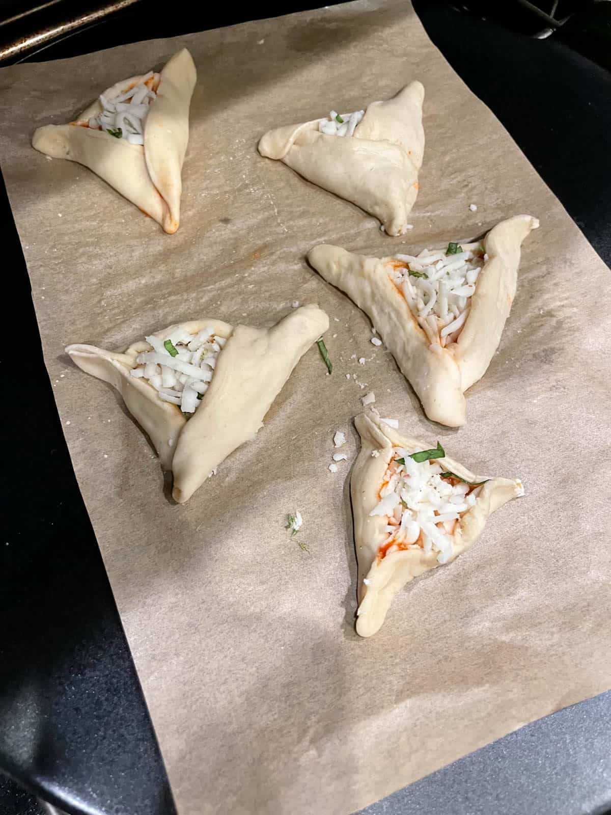 Folded hamantaschen pizzas on parchment paper.