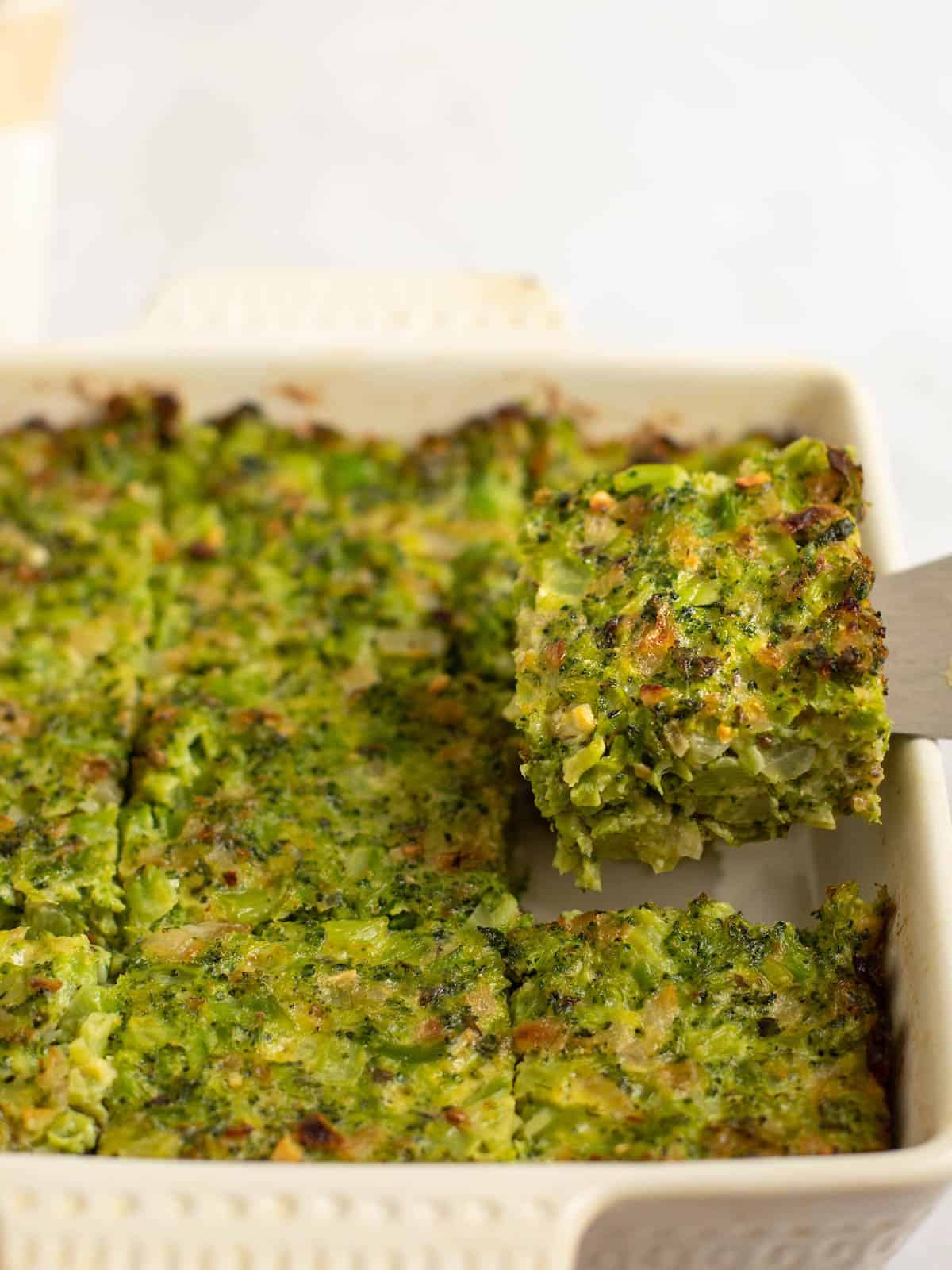 Scooping a serving of broccoli kugel out of a casserole dish.