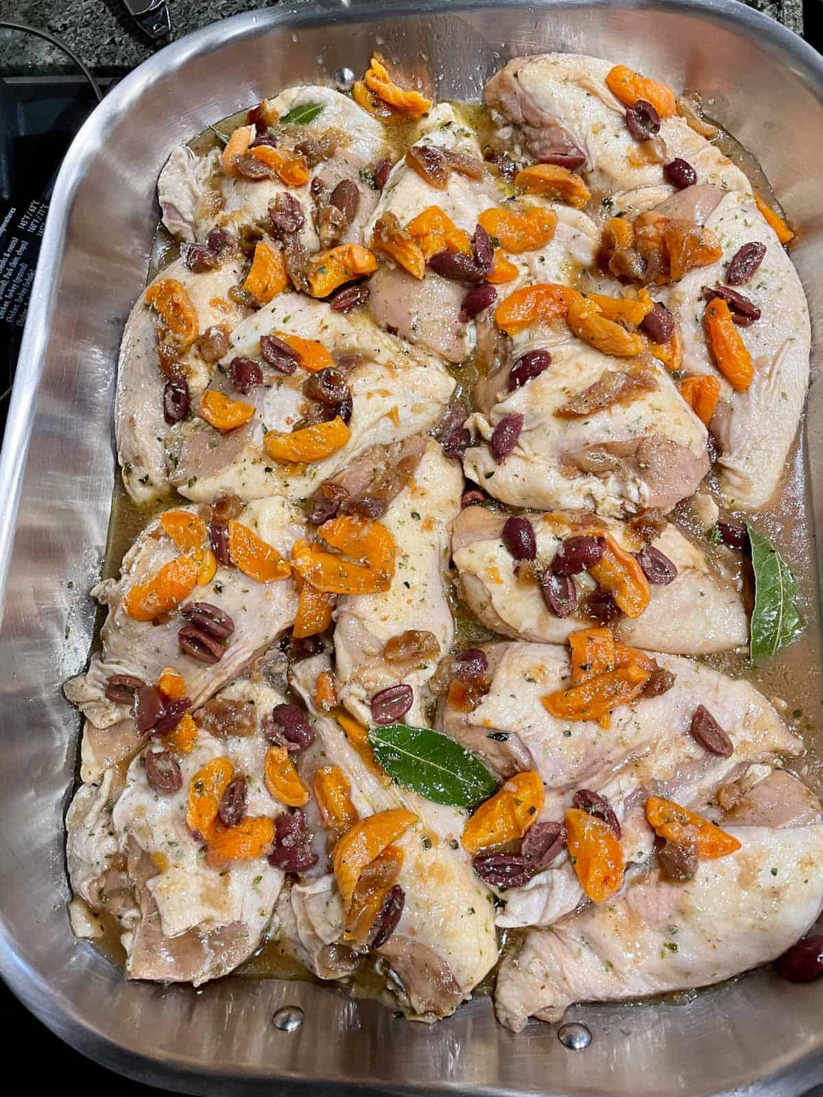 Chicken breasts with marinade and olives in a baking dish.