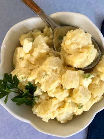 Potato salad in a white bowl with a spoon and blue background.