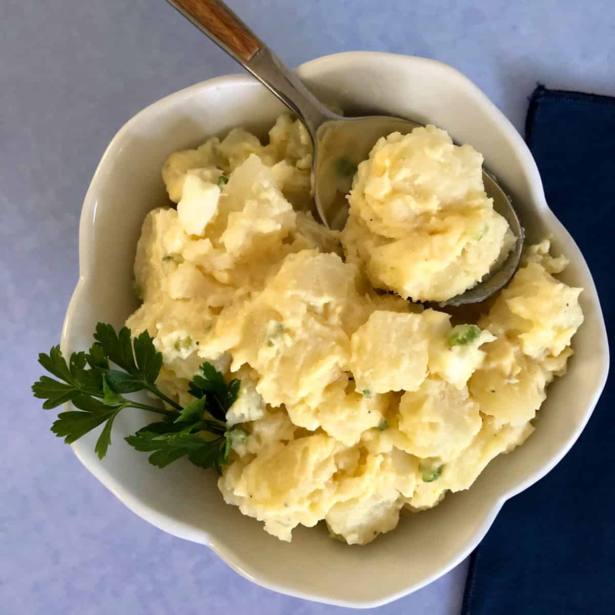 Potato salad in a white bowl with a spoon and blue background.
